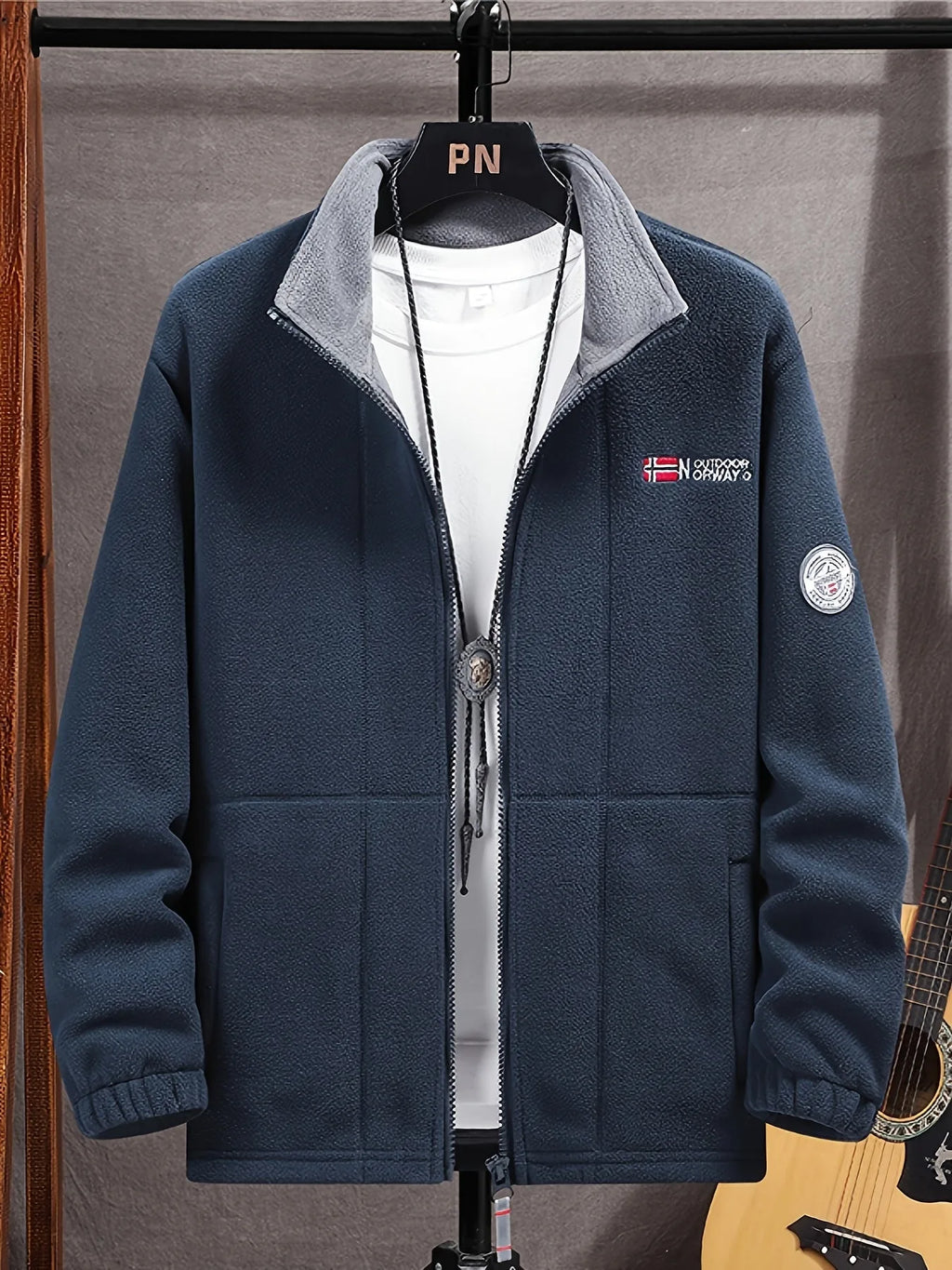 Navy fleece jacket on a hanger over a white t-shirt, showing the stand collar and embroidered flag logo