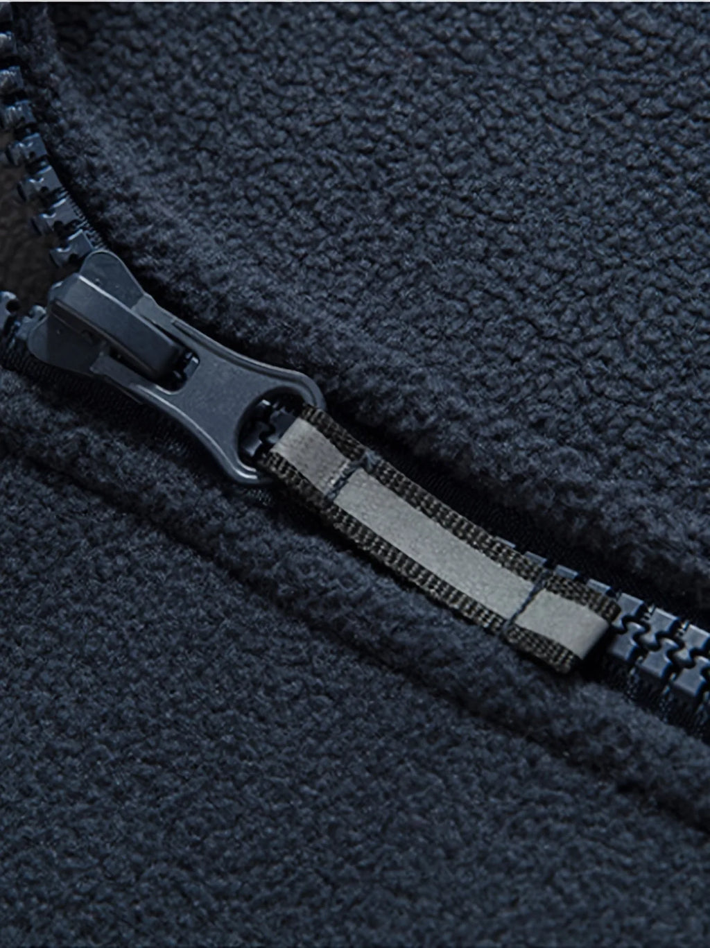 Close-up of the navy zip pull and reflective tab detail on the front zipper