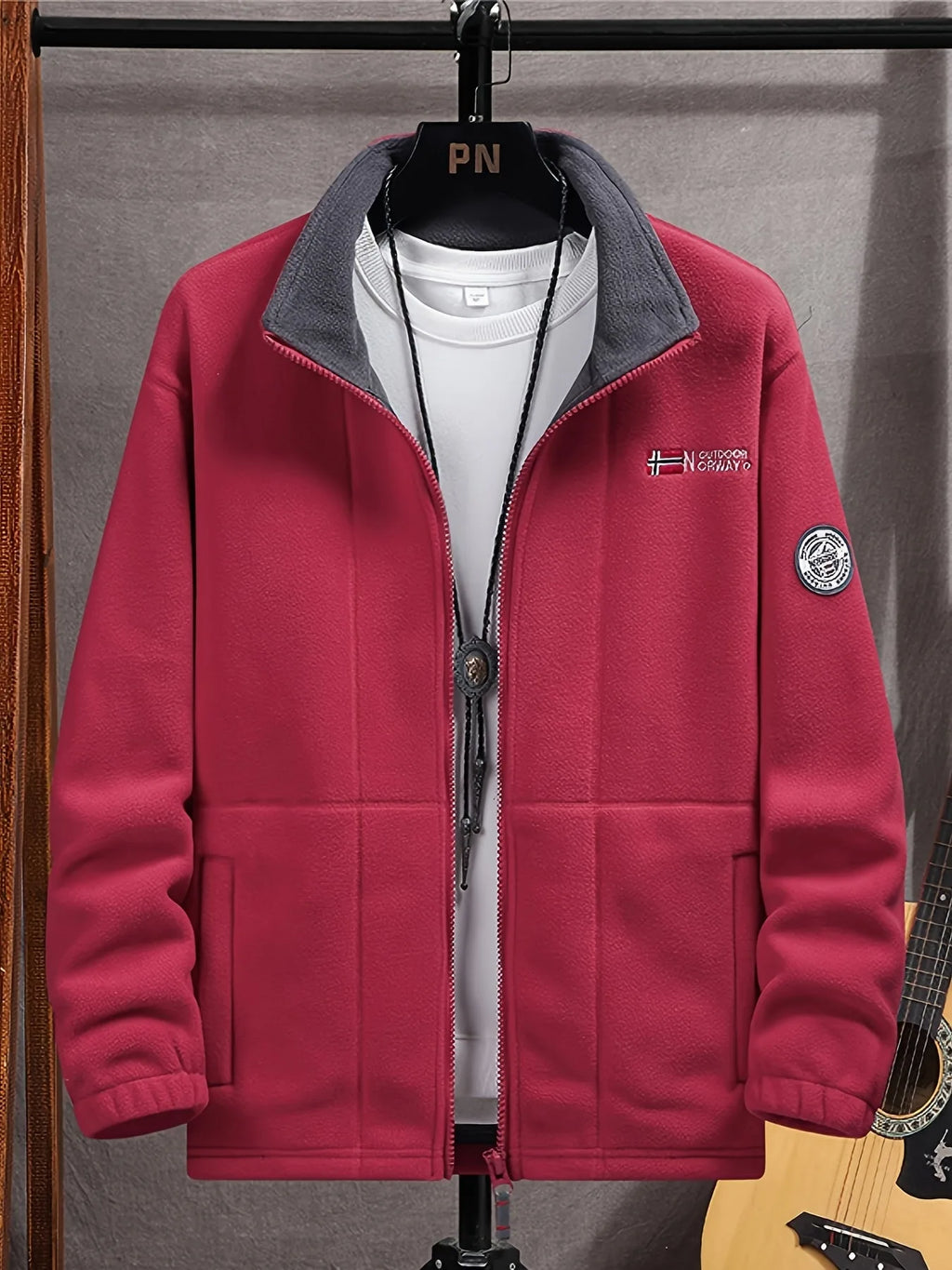 Burgundy red fleece jacket on a hanger over a white t-shirt, showing the collar and sleeve patch
