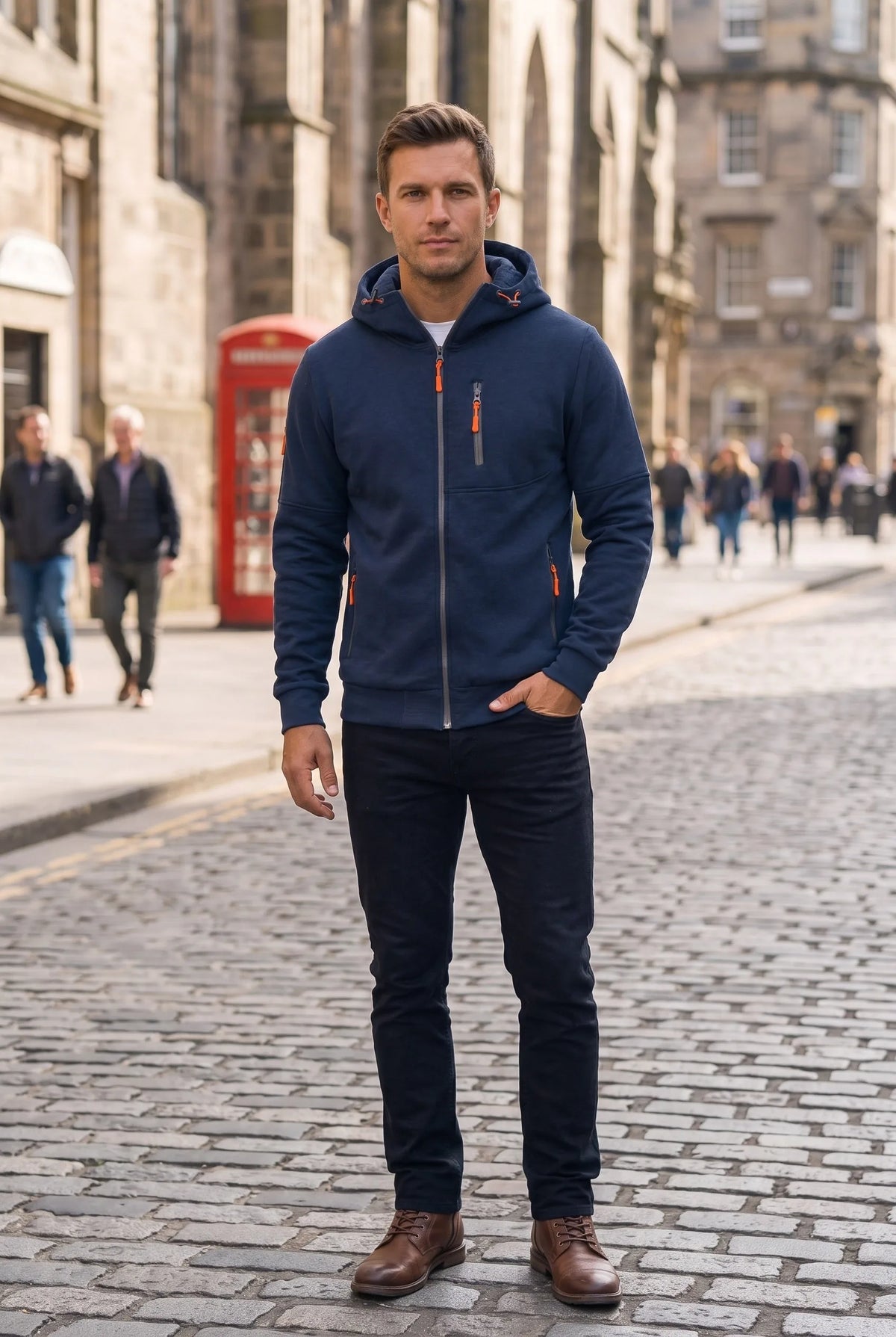 Man wearing a navy blue hoodie with jeans and boots while walking down a cobbled city street