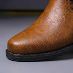 Close-up of the round toe cap on a cognac brown leather boot showing natural grain texture and stitched seam