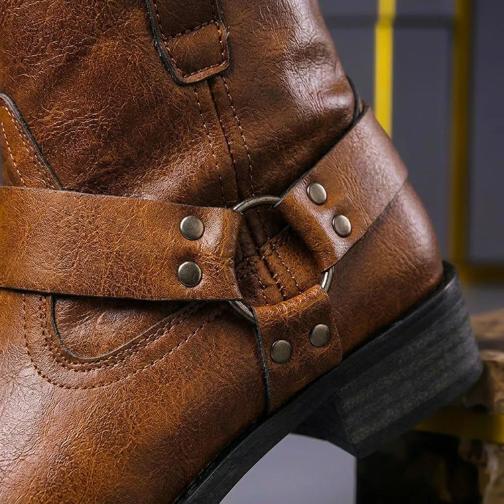 Detailed close-up of the riveted harness strap and metal ring on the back of a cognac brown leather boot