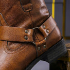 Detailed close-up of the riveted harness strap and metal ring on the back of a cognac brown leather boot