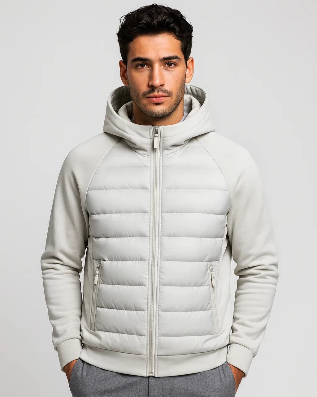 Front view of a man wearing a light grey hooded puffer jacket with quilted panel and softshell sleeves, zipped up