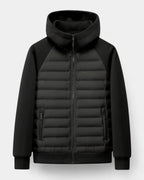Front view of the jacket in black, laid flat, showing quilted panel, zip pockets and softshell sleeves