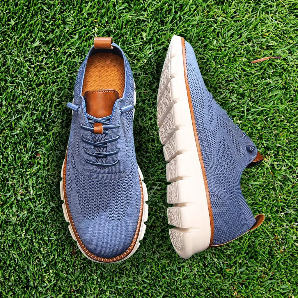 Blue knit lace-up trainer with tan leather heel pull shown on a grass background