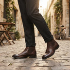 Man walking down a cobbled street wearing dark brown leather Chelsea boots with turned-up tailored trousers