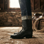 Cropped shot of a model wearing black cowboy boots with rolled denim jeans in a rustic barn setting