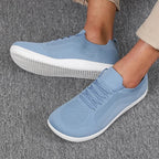 Side view of light blue knit trainers worn on feet, showing lace-up front and white ridged sole