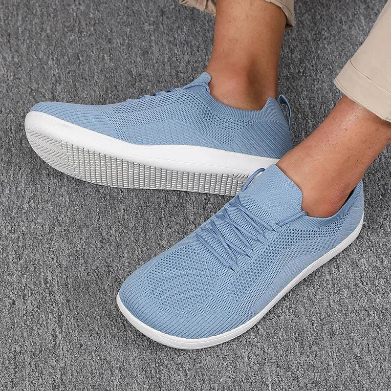 Side view of light blue knit trainers worn on feet, showing lace-up front and white ridged sole