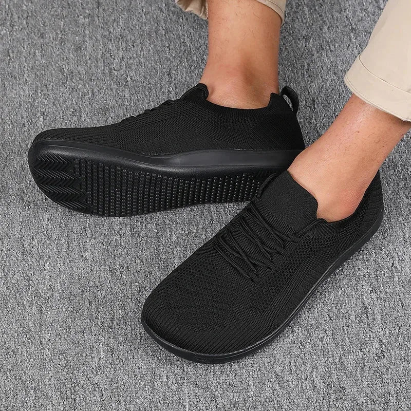 Angled view of men's black mesh trainers with lace detail and matching black ridged sole