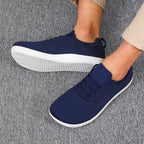 Side profile of navy knit trainers on feet with white sole and lace-up front panel