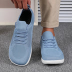 Hand holding one light blue knit trainer beside a foot wearing the matching pair