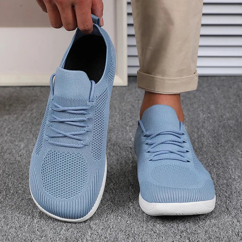 Hand holding one light blue knit trainer beside a foot wearing the matching pair