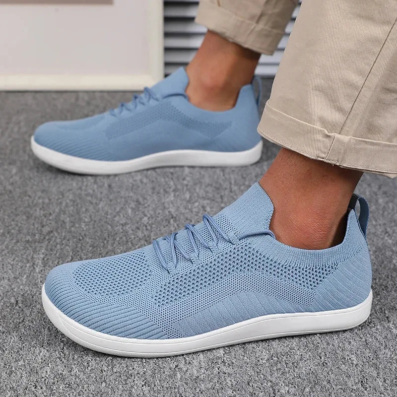 Hand lifting a light blue knit trainer by the heel loop next to a worn matching shoe