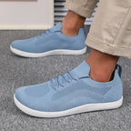 Hand lifting a light blue knit trainer by the heel loop next to a worn matching shoe
