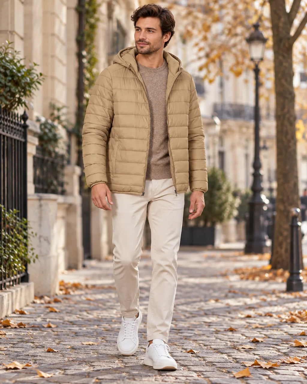 Man walking in a beige hooded puffer jacket with full-length zip, worn over a jumper with cream trousers and white trainers