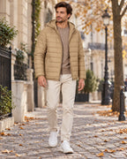 Man walking in a beige hooded puffer jacket with full-length zip, worn over a jumper with cream trousers and white trainers