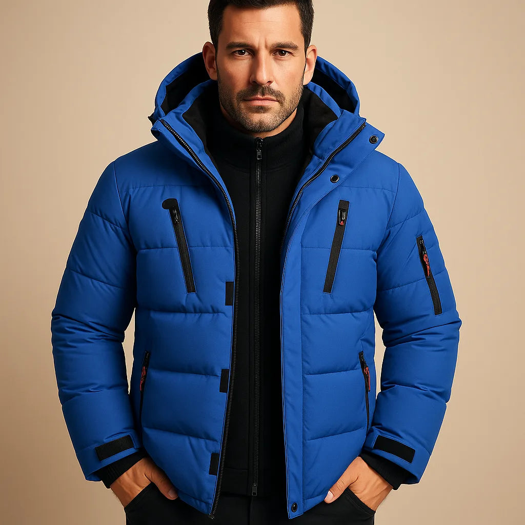 Man wearing a blue quilted puffer jacket with black zip pockets and a drawstring hood, shown from the front.