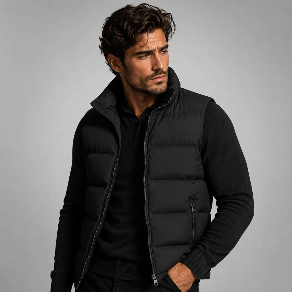 Man wearing a black quilted gilet open over a black polo neck jumper, hands in trouser pockets