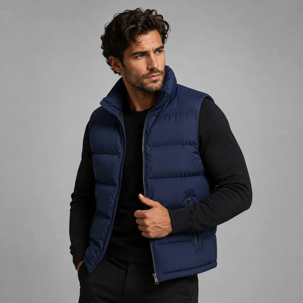 Man wearing an open navy blue quilted gilet over a black jumper, hands in trouser pockets
