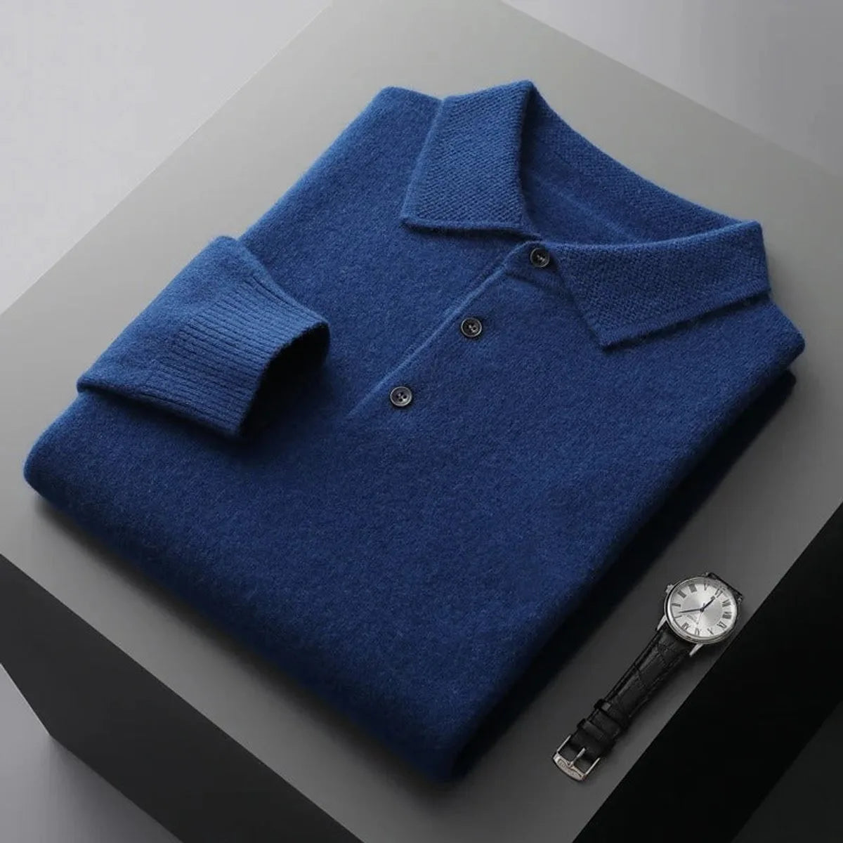Folded blue cashmere polo jumper with ribbed collar, button placket and cuffs shown beside a wristwatch