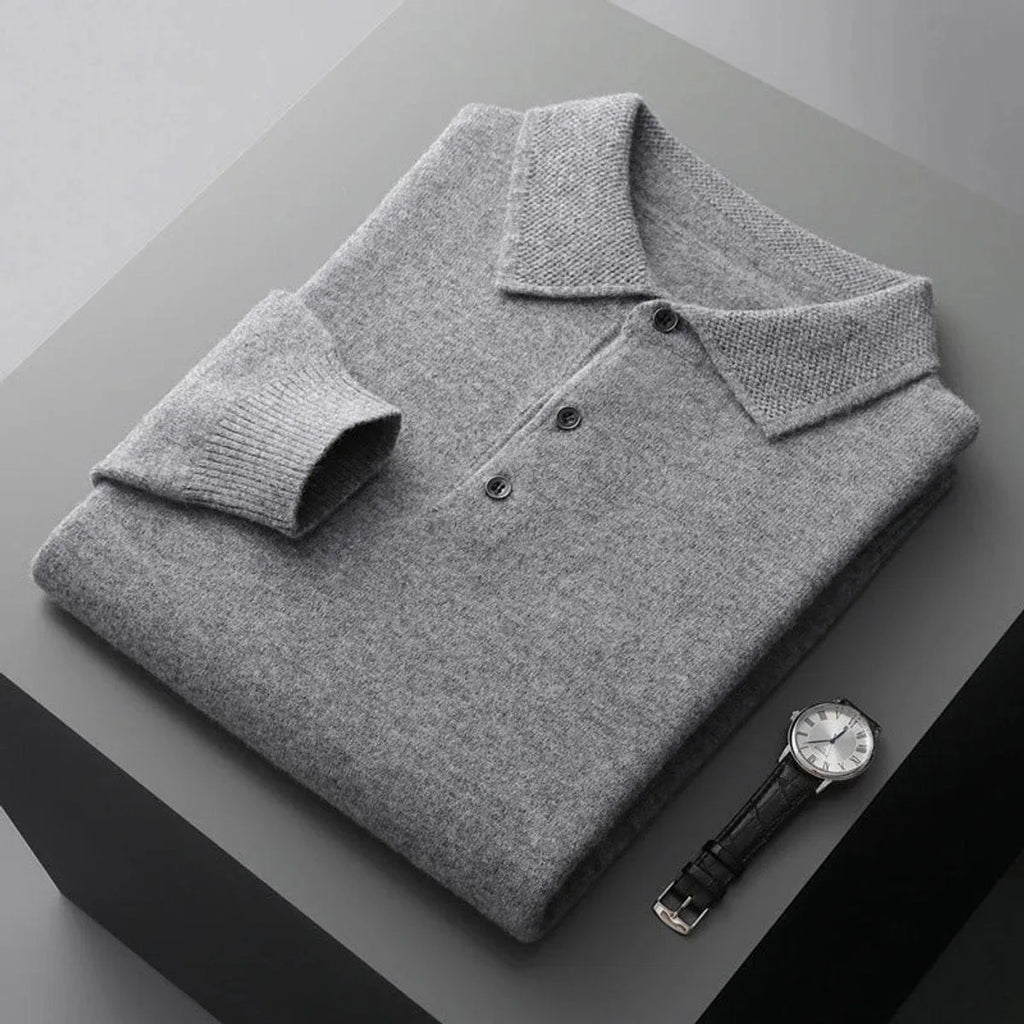 Folded grey marl cashmere polo jumper with textured collar and dark buttons on a two-tone surface