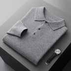 Folded grey marl cashmere polo jumper with textured collar and dark buttons on a two-tone surface