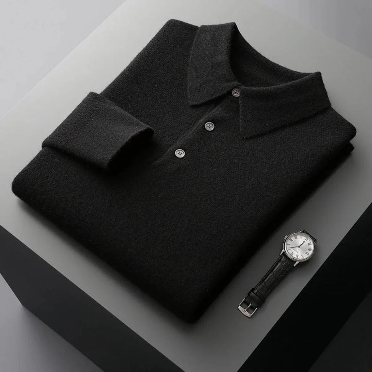 Folded black cashmere polo jumper with matching buttons and ribbed collar on a dark backdrop