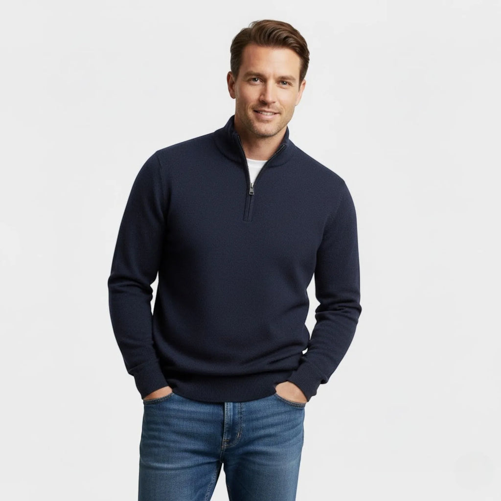 Man wearing a navy textured quarter-zip jumper with a white tee underneath and jeans, hands in pockets