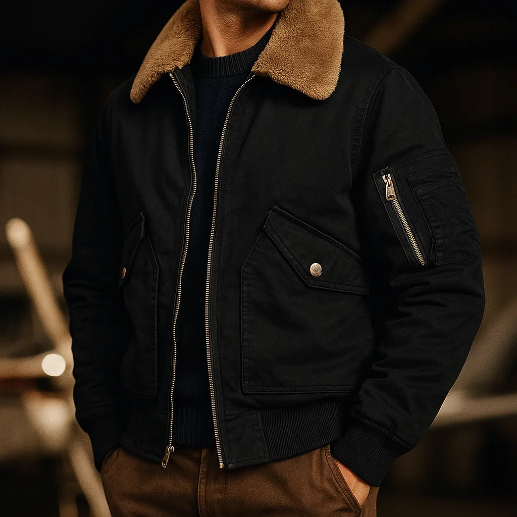 Black bomber jacket with tan shearling collar worn open over a dark jumper, sleeve zip pocket visible