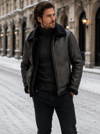 Man wearing a black leather aviator jacket with black shearling collar, zipped partway over a black polo neck.