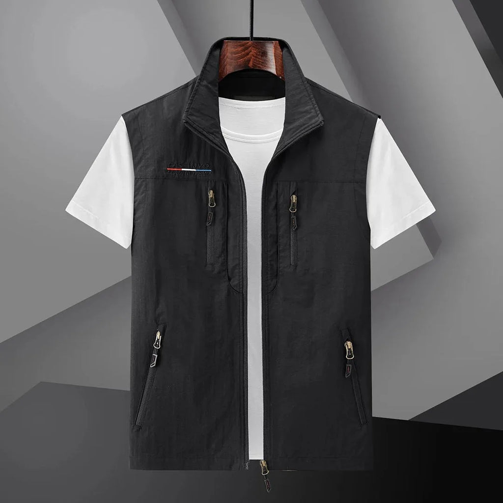 Black sleeveless zip-up gilet with stand collar and multiple zip pockets, shown open over a white t-shirt on a hanger
