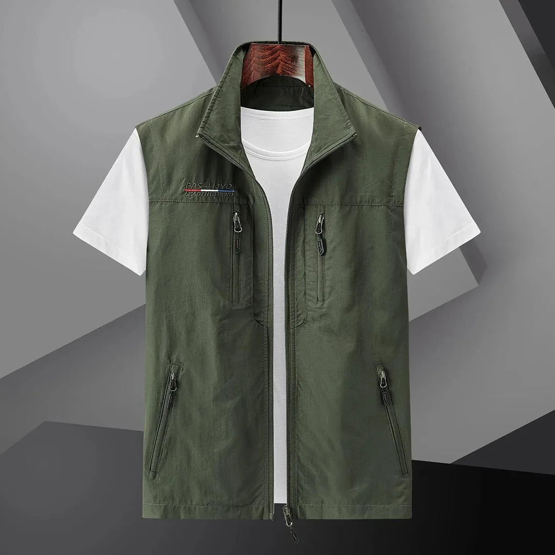 Olive green sleeveless zip-up gilet with front zip and four zip pockets, worn open over a white t-shirt