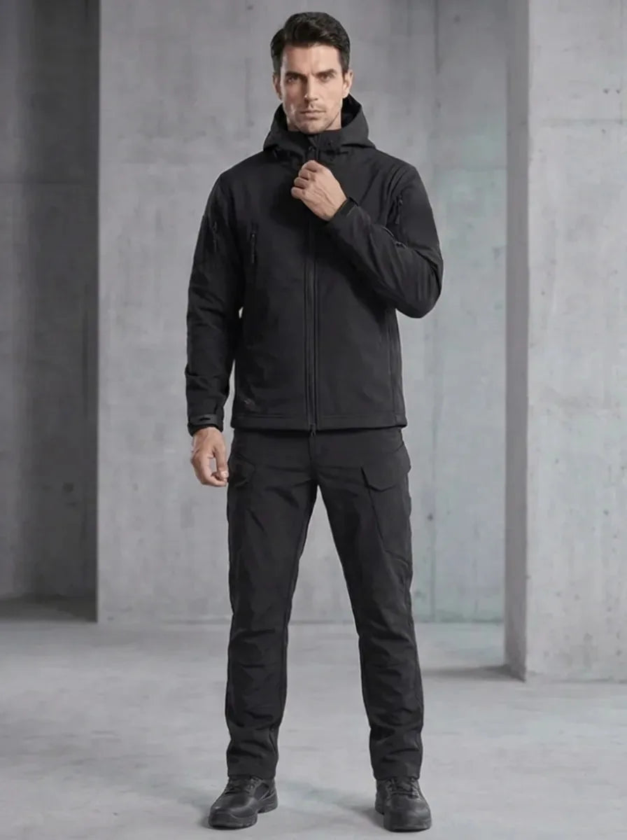 Man wearing a black softshell hooded jacket and matching cargo trousers with tactical boots, front view