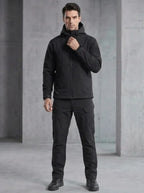 Man wearing a black softshell hooded jacket and matching cargo trousers with tactical boots, front view