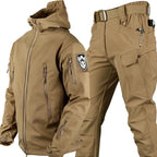 Tan softshell jacket with hood and matching cargo trousers, front view showing zips, patch and belt buckle
