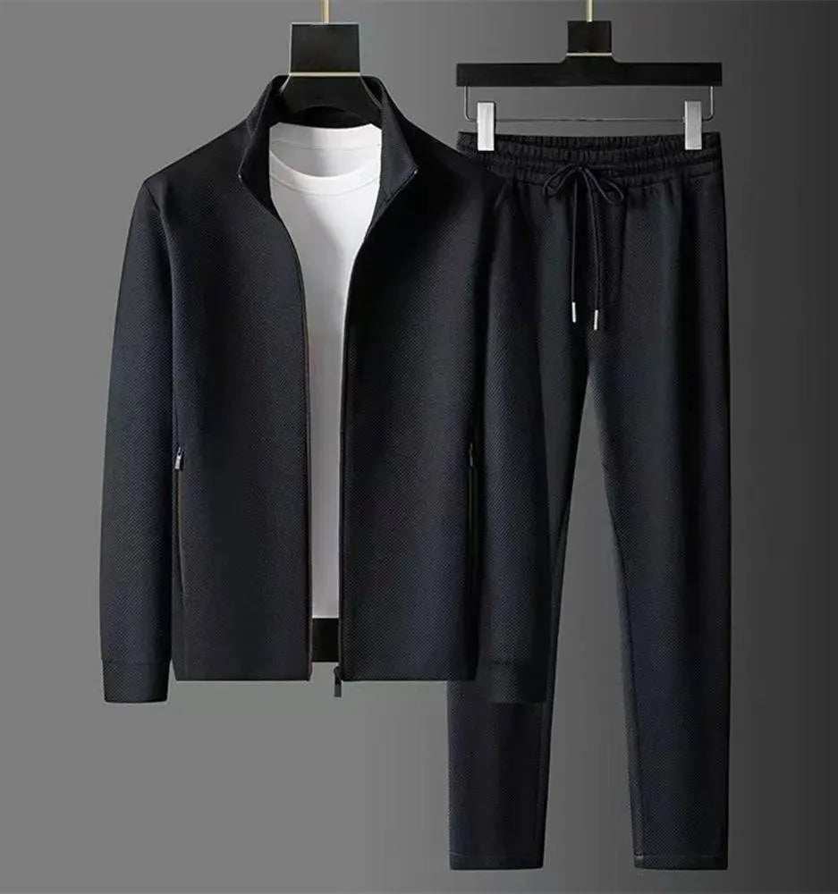 Full black tracksuit set shown together on hangers, zip-up jacket with stand collar and matching trousers