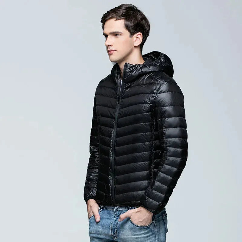 Side profile of a man wearing a glossy black ultralight puffer jacket with hood up, paired with jeans