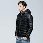 Side profile of a man wearing a glossy black ultralight puffer jacket with hood up, paired with jeans