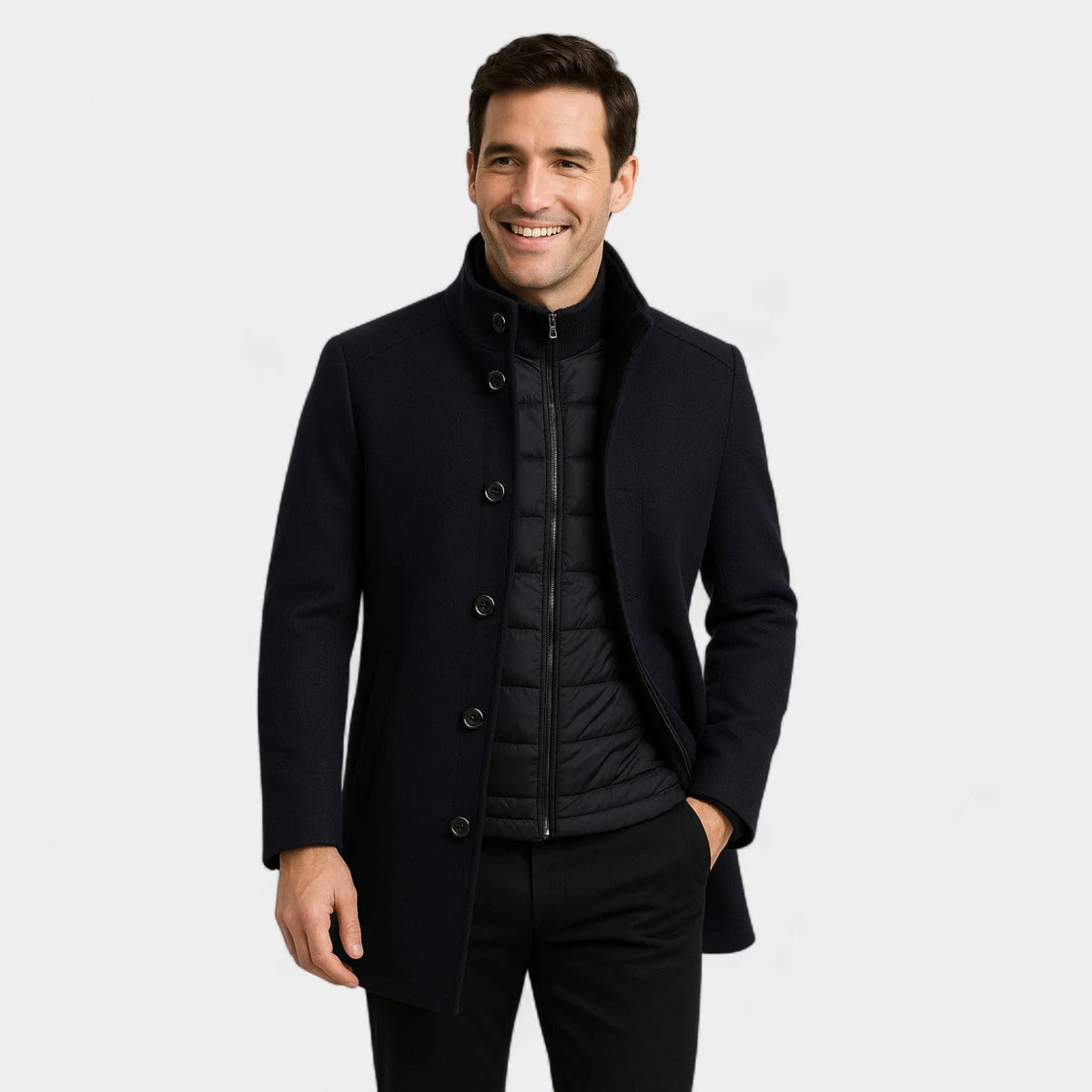 Man wearing a navy wool-blend coat with a stand collar, buttoned front and zipped quilted inner gilet, hands relaxed at his side