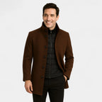 Man smiling in a chocolate brown wool-blend coat worn open over a black gilet, showing the single-breasted button front