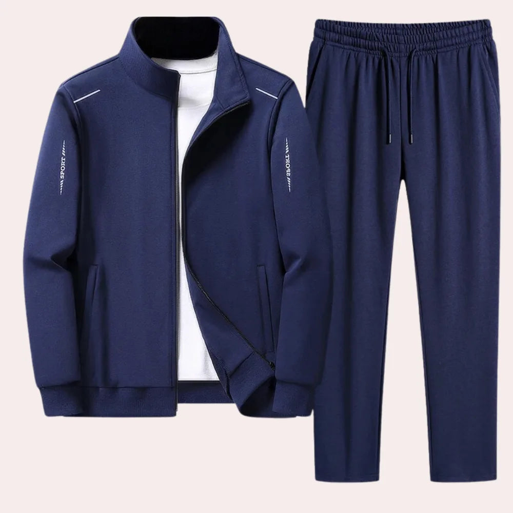 Navy blue zip-up tracksuit jacket with stand collar worn over a white t-shirt, paired with matching navy joggers