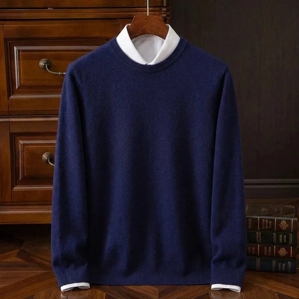 Navy blue crew neck jumper with ribbed collar and cuffs, displayed on a wooden hanger against a dark panelled wall