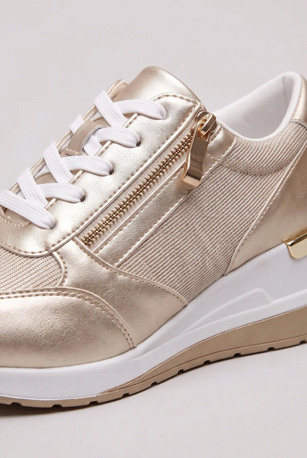 Close-up of gold metallic trainer showing the side zip pull, elastic panel and stitched toe cap detail