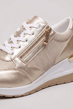 Close-up of gold metallic trainer showing the side zip pull, elastic panel and stitched toe cap detail