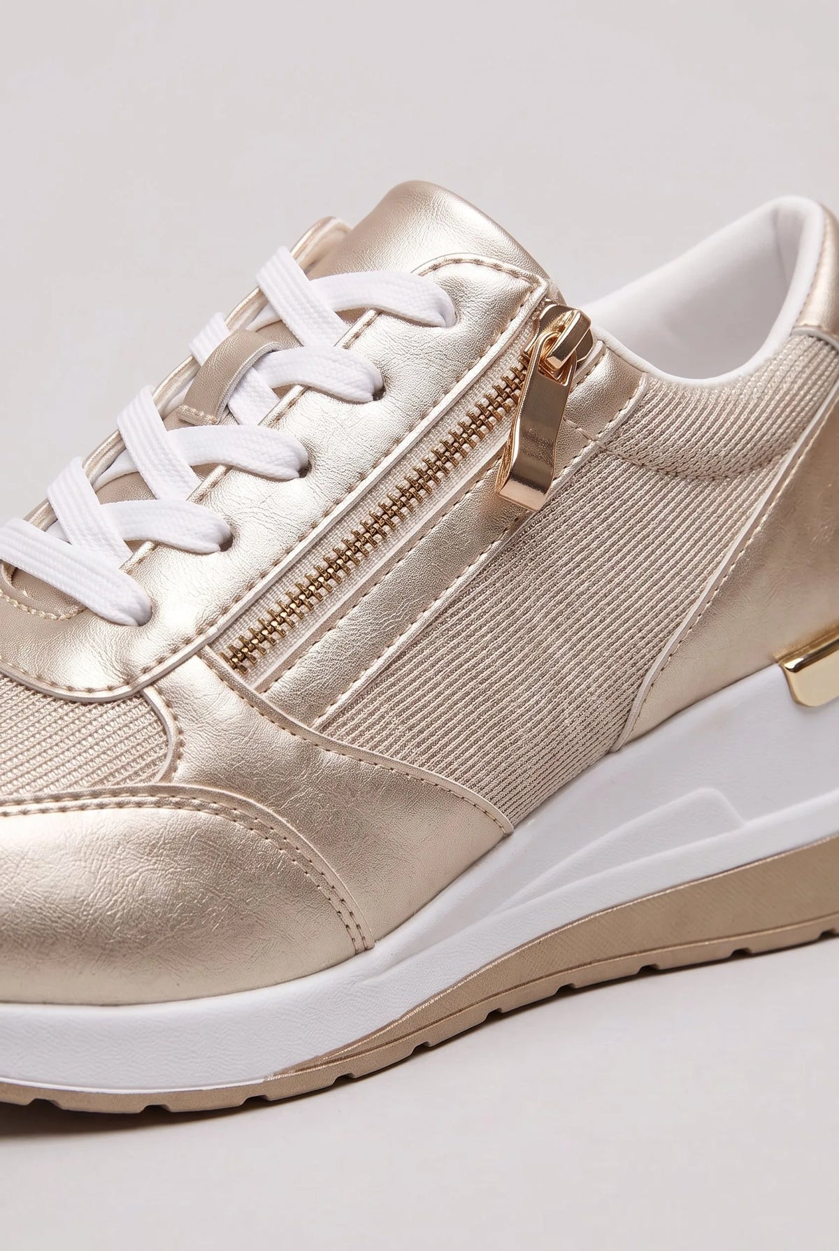Close-up of gold metallic trainer showing the side zip pull, elastic panel and stitched toe cap detail