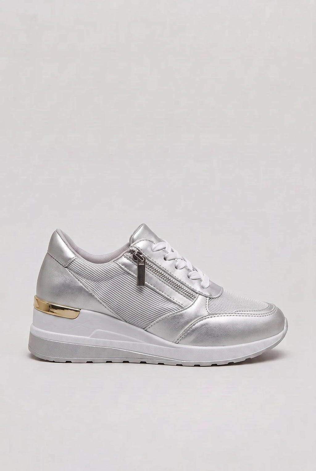 Side view of silver metallic wedge trainer with white laces, side zip and gold heel trim on a white wedge sole