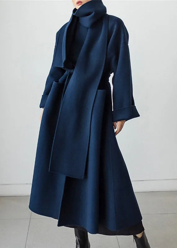 Front angled view of a navy polo neck maxi coat with wraparound scarf-style collar and tie waist, worn open over a black outfit
