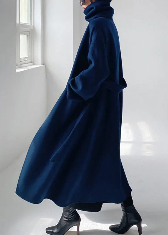 Side profile of the oversized navy coat in motion, showing the flowing A-line hem and folded polo neck